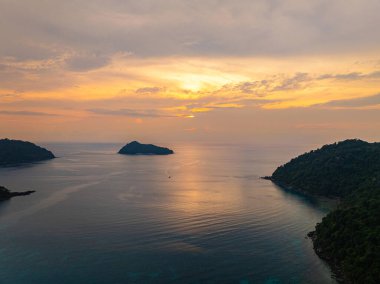 Güneşin Ao Mai Ngam, Surin Adaları 'ndan batışını gösteren hava manzarası. Batan güneşin yansıması. Bereketli yeşil tepeler ve demirlemiş yelkenlilerin silueti huzurlu ortamı geliştirirken.