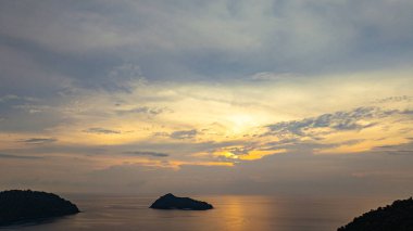 Surin Adaları üzerinde çarpıcı bir günbatımının havadan görüntüsü. Sakin okyanus sularına yansıyan altın renklerle. Sahil şeridindeki mercan resifi derinlik katıyor. Şnorkel için cennet