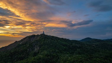 Phuket, Tayland 'daki Andaman Denizi' ne bakan ikonik Büyük Buda heykelinin canlı bir günbatımında çekilmiş nefes kesici bir görüntüsü. Altın gökyüzü suyu yansıtır. Güzel güneş