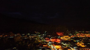 Geceleri sıcak altın ışıklarla aydınlatılmış göldeki bir köyün çarpıcı hava manzarası. Yüzen fenerler ve tekneler, Baan Rak Tayland usulü karanlık sularda büyüleyici bir desen oluşturur.