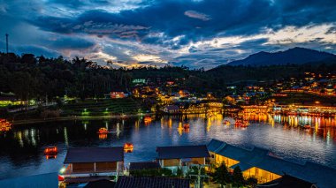 Baan Rak Tayland Köyü, gün batımında Çin tarzı mimaride göl kenarındaki ev ve restoranların renkli ışıklarla yansıması. Mae Hong Son 'da popüler bir turizm merkezi.