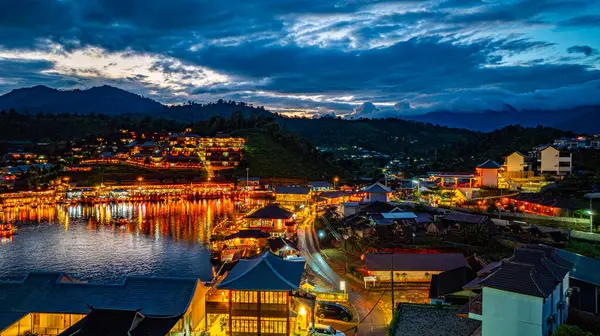 Baan Rak Tayland Köyü, gün batımında Çin tarzı mimaride göl kenarındaki ev ve restoranların renkli ışıklarla yansıması. Mae Hong Son 'da popüler bir turizm merkezi.
