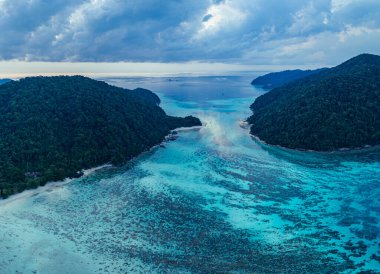 Turkuaz okyanus bulutların altında yemyeşil adalarla buluşuyor.