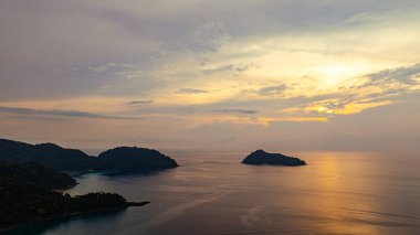 Surin Adaları üzerinde çarpıcı bir günbatımının havadan görüntüsü. Sakin okyanus sularına yansıyan altın renklerle. Sahil şeridindeki mercan resifi derinlik katıyor. Şnorkel için cennet