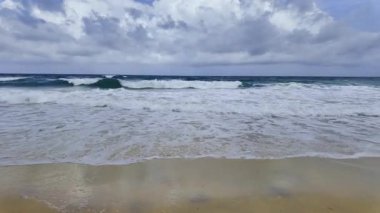 Dalgalar bulutların altında kumsala çarpıyor.