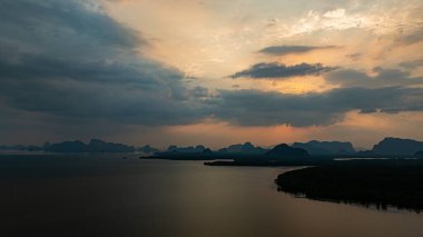 Phang Nga 'nın kireçtaşı dağlarının pembe ve altın bulutlara karşı gölgelenmiş muhteşem gündoğumu manzarası. Tropikal mangrov ormanı aşağıda uzanır ve canlı bir doğal manzara çizer..