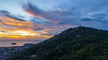 Phuket, Tayland 'daki Andaman Denizi' ne bakan ikonik Büyük Buda heykelinin canlı bir günbatımında çekilmiş nefes kesici bir görüntüsü. Altın gökyüzü suyu yansıtır. Güzel güneş