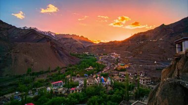 Gün batımında yeşil tepelerin arasında yuva yapmış renkli bir köy.