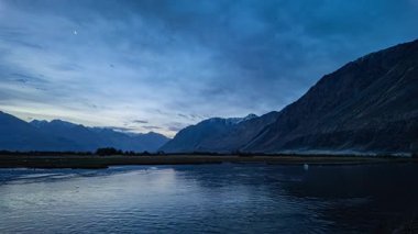 Sakin göl, dağların yakınında mavi gökyüzünü yansıtıyor.