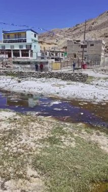 Taştan binaların yanında sığ nehir kıyısında duran insanlar.