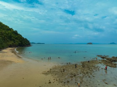 İnsanlar sakin turkuaz suyun yakınındaki kumsalın tadını çıkarıyorlar.