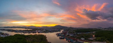 Phuket 'teki balıkçı limanında sersemletici gün batımını gösteren hava manzarası. Yumuşak mor renkten ateşli turuncu renklere dönüşen canlı gökyüzü, sakin ve pitoresk bir atmosfer yaratır..  