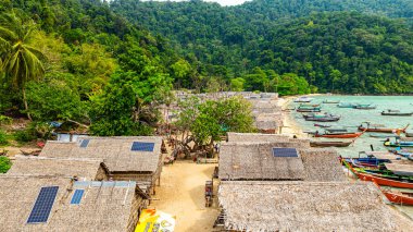 Phang Nga, Tayland-Mart, 20.2025: Yeşillik yeşil ormanlarla çevrili kıyı şeridi boyunca sıralanmış küçük kulübeleriyle tropikal bir sahil Morgan köyünün çarpıcı hava manzarası. Balıkçı tekneleri demirli.