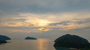Surin Adaları üzerinde çarpıcı bir günbatımının havadan görüntüsü. Sakin okyanus sularına yansıyan altın renklerle. Sahil şeridindeki mercan resifi derinlik katıyor. Şnorkel için cennet