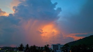 Canlı ve dinamik bir gökyüzü, batan güneşin sıcak renkleriyle aydınlanan yüksek fırtına bulutlarını yakalar ve karanlık bir ormanın üzerindeki ışık ile gölge arasında çarpıcı bir kontrast yaratır..
