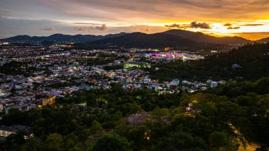 Gökyüzünü, Khao Rang 'ın üzerindeki altın ve turuncu renklerle dolduran, tepelerin doğal hatlarını ve aşağıdaki kentsel manzaranın sessiz çekiciliğini vurgulayan, ışıl ışıl bir gün batımı manzarası.