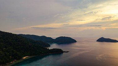 Surin Adaları üzerinde çarpıcı bir günbatımının havadan görüntüsü. Sakin okyanus sularına yansıyan altın renklerle. Sahil şeridindeki mercan resifi derinlik katıyor. Şnorkel için cennet