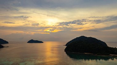 Surin Adaları üzerinde çarpıcı bir günbatımının havadan görüntüsü. Sakin okyanus sularına yansıyan altın renklerle. Sahil şeridindeki mercan resifi derinlik katıyor. Şnorkel için cennet