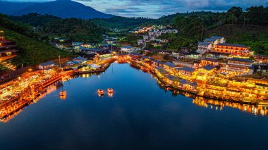 Baan Rak Tayland Köyü, gün batımında Çin tarzı mimaride göl kenarındaki ev ve restoranların renkli ışıklarla yansıması. Mae Hong Son 'da popüler bir turizm merkezi.