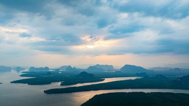 Phang Nga 'nın kireçtaşı dağlarının pembe ve altın bulutlara karşı gölgelenmiş muhteşem gündoğumu manzarası. Tropikal mangrov ormanı aşağıda uzanır ve canlı bir doğal manzara çizer..