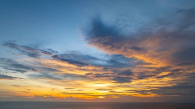 Nefes kesen bir günbatımı, kıyı kasabasının üzerinde turuncu ve mavi renkli canlı renkler çiziyor. Sahneyi çevreleyen yemyeşil tepeler var. Uzak bir tepe yapısı huzur dolu bir manzara ekler..  