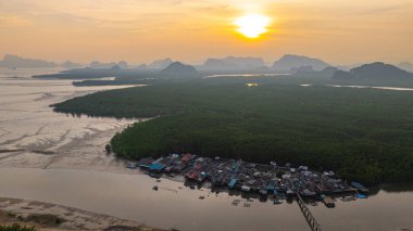 Bereketli mangrovlarla çevrili yüzen bir köyün nefes kesici hava manzarası. Güneş uzak kireçtaşı dağlarının ardında batıyor. Altın ışık sakin suları yansıtır. Bangpat Adası