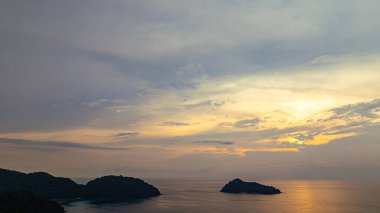 Surin Adaları üzerinde çarpıcı bir günbatımının havadan görüntüsü. Sakin okyanus sularına yansıyan altın renklerle. Sahil şeridindeki mercan resifi derinlik katıyor. Şnorkel için cennet