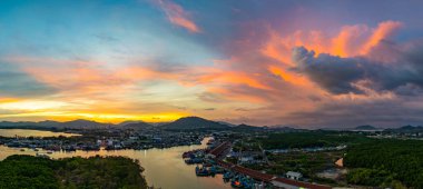 Phuket 'teki balıkçı limanında sersemletici gün batımını gösteren hava manzarası. Yumuşak mor renkten ateşli turuncu renklere dönüşen canlı gökyüzü, sakin ve pitoresk bir atmosfer yaratır..  