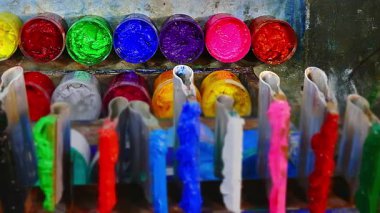 Bir ekran baskı dükkanındaki ahşap tezgahta, çeşitli plastisol mürekkep kutuları açık, zengin tonlarda yumuşak pasteller, güçlü primatlar ve derin gölgeler ortaya çıkıyor. Yakınlarda bir tahta kaşık ve mala dinleniyor..