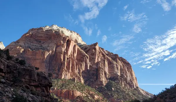 This photo captures the awe-inspiring beauty of a mountain in Zion National Park. The red rock formations and desert landscape create a stunning backdrop for the blue sky and clouds. This is a must-visit destination for nature lovers and adventurers.