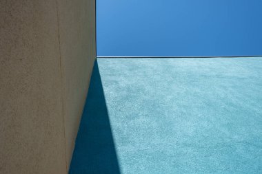 Turkuaz ve bej duvarlı bir binanın köşesinin soyut mimari ayrıntıları, koyu bir gölge ve tepede parlak mavi bir gökyüzü..