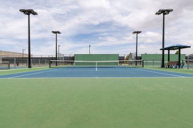 An empty public tennis court during the day with a partly cloudy sky. clipart