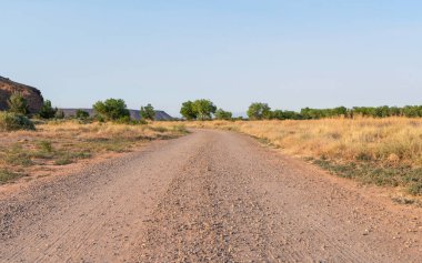 Yüksek çöl kırsalında kızıl kayaların yanında boş bir toprak yol kıvrılır..