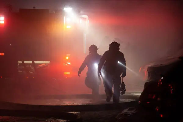 Silhouette of firefighters walking way from smoke with flashlights on their chest