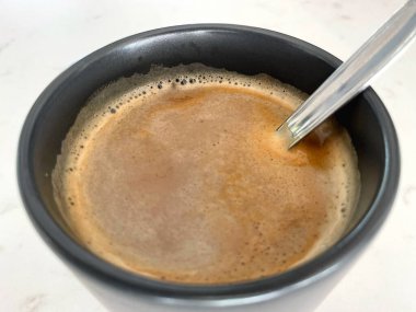 Close-Up of Coffee Foam in Dark Ceramic Mug with Spoon clipart