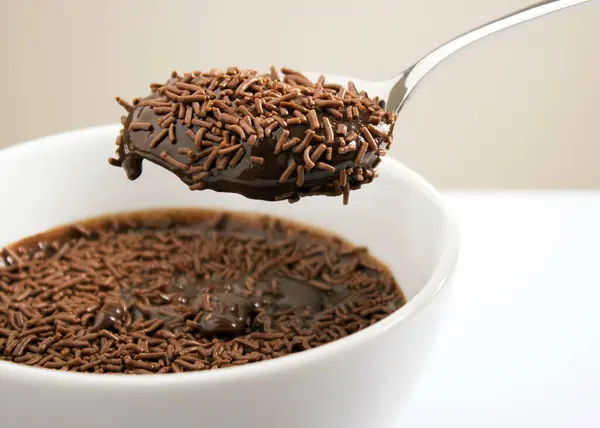 Spoon brigadeiro with sprinkles, Brazilian food, in a white bowl and blurred background, close up, front