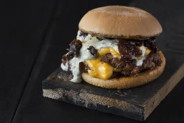 fast food, burger, brioche bun, cheddar cheese, red meat and caramelized onion with mayonnaise, dark background, rustic wood