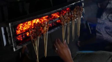 Geleneksel kömür ateşinde tavuk satay. Duman ve iştah açıcı bir bakışla alev alev yanıyordu. Eller ızgarada satay pişiriyor, dikey video.