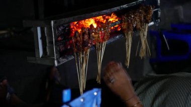 Geleneksel kömür yangınında Chicken Satay 'in dikey videosu. Duman ve iştah açıcı bir bakışla alev alev yanıyordu. Eller ızgarada satay pişiriyor.