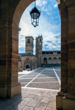 Çan kulesi ve kilise olan taştan bir kemerle çerçevelenmiş bir kare manzarası.