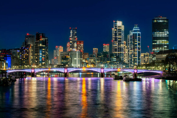 Современная панорама Лондона ночью с красочными огнями, отражающимися на Темзе и освещенным мостом на переднем плане