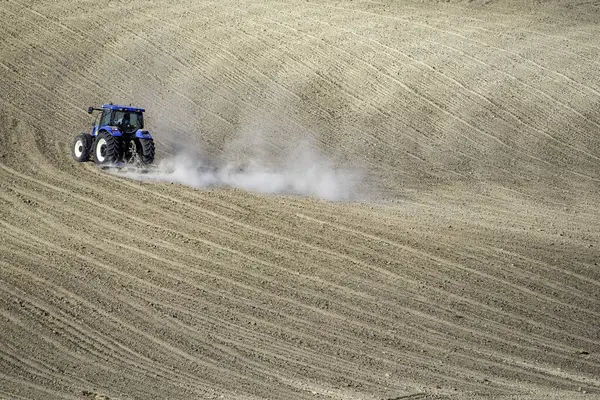 Bir traktör yeni sürülmüş dalgalı topraklarda hareket ederek, minimalist bir arazide tarım makinelerini ve kırsal verimliliği vurguluyor.