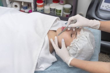 Estetik bir merkezde sedyede yatan genç bir kadın cilt bakımı ve neşter cilt bakımı teknikleriyle yüz güzelliği ve estetik tedavi uyguluyor.