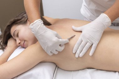 Estetik bir merkezde sedyede yatan genç bir kadın cilt bakımı ve neşterle cilt bakımı teknikleri ile yüz ve vücut güzelliği ve estetik tedavi uyguluyor.