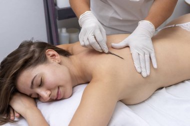 Estetik bir merkezde sedyede yatan genç bir kadın cilt bakımı ve neşterle cilt bakımı teknikleri ile yüz ve vücut güzelliği ve estetik tedavi uyguluyor.