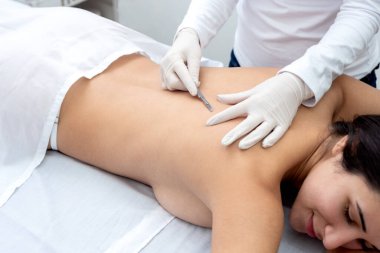 Estetik bir merkezde sedyede yatan genç bir kadın cilt bakımı ve neşterle cilt bakımı teknikleri ile yüz ve vücut güzelliği ve estetik tedavi uyguluyor.