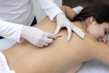 Estetik bir merkezde sedyede yatan genç bir kadın cilt bakımı ve neşterle cilt bakımı teknikleri ile yüz ve vücut güzelliği ve estetik tedavi uyguluyor.