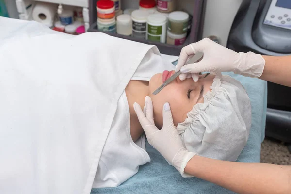 Estetik bir merkezde sedyede yatan genç bir kadın cilt bakımı ve neşter cilt bakımı teknikleriyle yüz güzelliği ve estetik tedavi uyguluyor.
