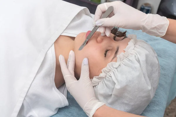 young woman lying on a stretcher in an aesthetic center performing facial beauty and aesthetic treatment with dermapen and scalpel dermaplaning techniques
