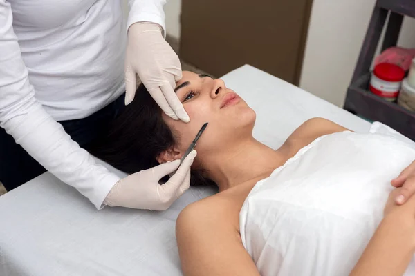 young woman lying on a stretcher in an aesthetic center performing facial and body beauty and aesthetic treatment with dermapen and dermaplaning techniques with scalpel